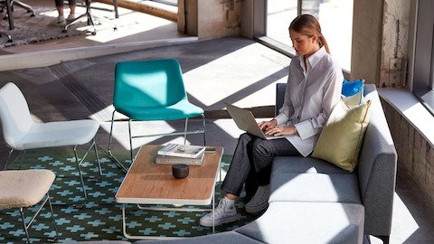 Uma mulher sentada em um assento modular Symbol, usando um laptop. Uma mulher sentada em um assento modular Symbol, usando um laptop.