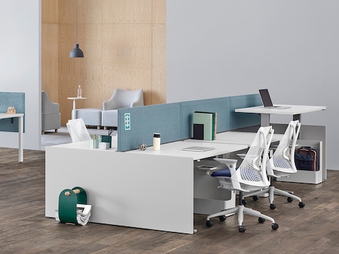 Una oficina con estaciones de trabajo Canvas Channel con pantallas de tejido azul y escritorios blancos junto a un área de sillas lounge.