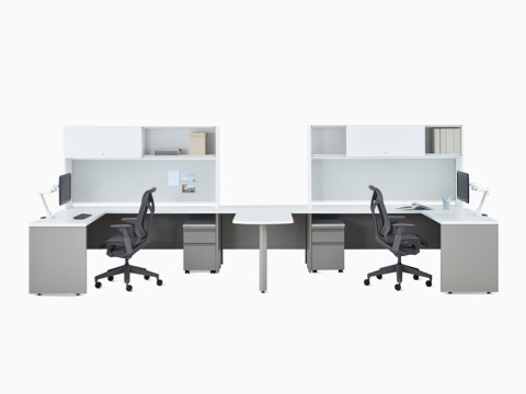 Dos escritorios metálicos Canvas en blanco y gris con almacenamiento superior, brazo articulado para monitor Concerto y silla Cosm en gris oscuro.