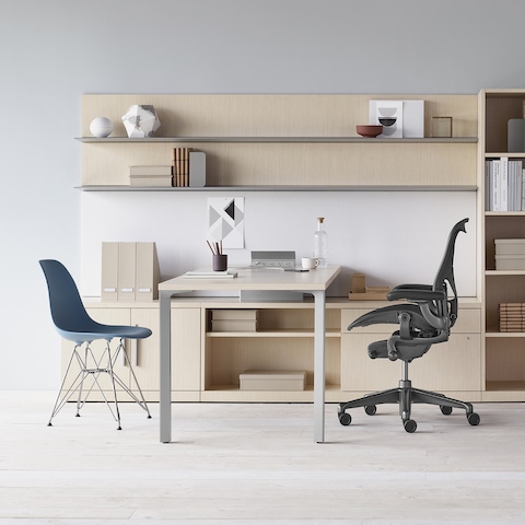 Mesa Canvas Private Office com armário em madeira clara, prateleiras superiores, cadeira de escritório Aeron preta e cadeira azul sem braços em plástico moldado Eames.