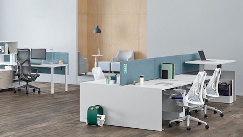 Una oficina con estaciones de trabajo Canvas Channel y Canvas Dock con pantallas de tela en azul y escritorios en blanco cerca de un área de sillas lounge.