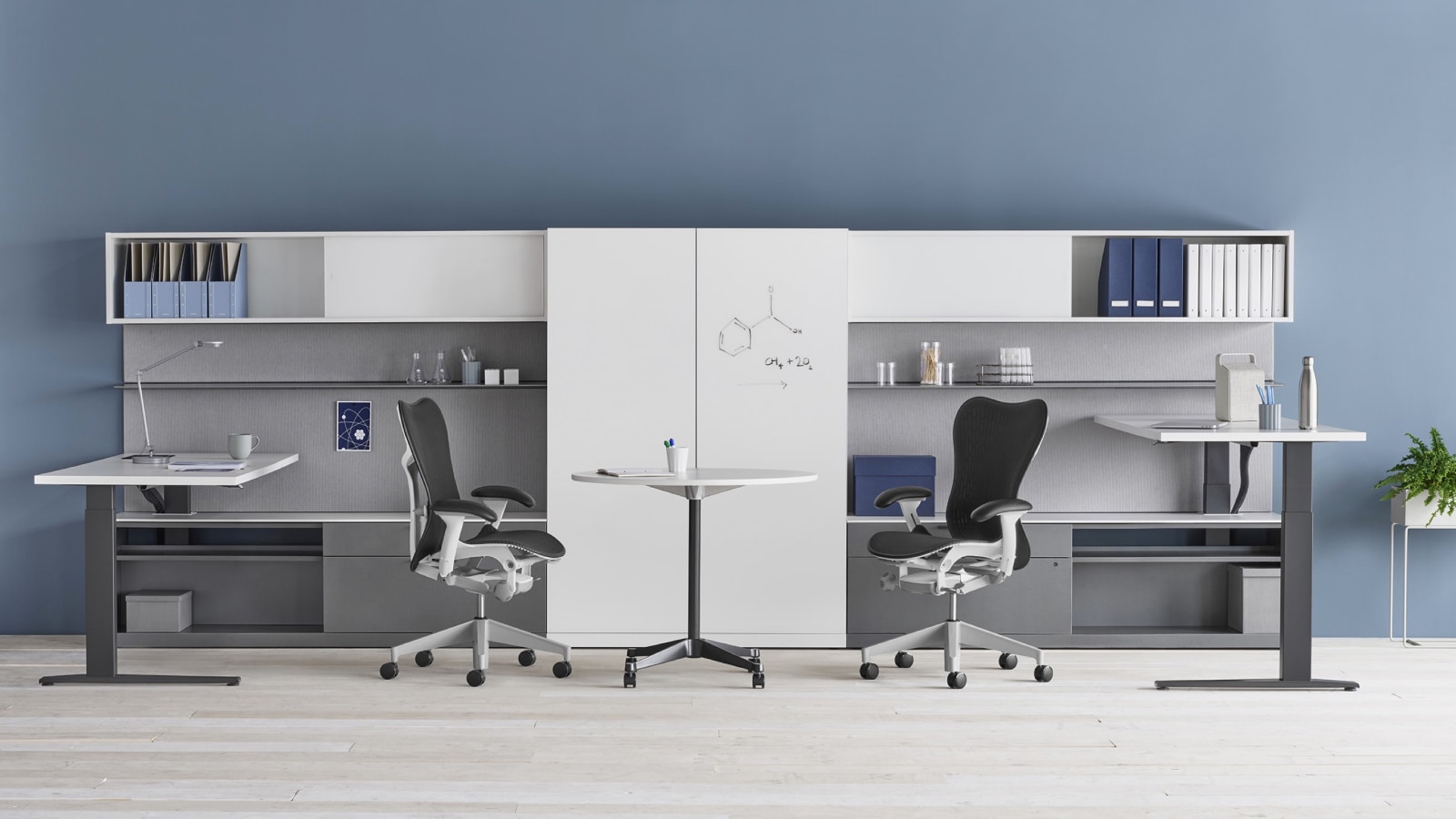 A shared Canvas Private Office with white and gray storage, one standing desk at seated height and one standing desk at standing height, and dark gray Mirra 2 office chairs. Select to go to the Impromptu Meeting Spaces page within the Canvas Lookbook.