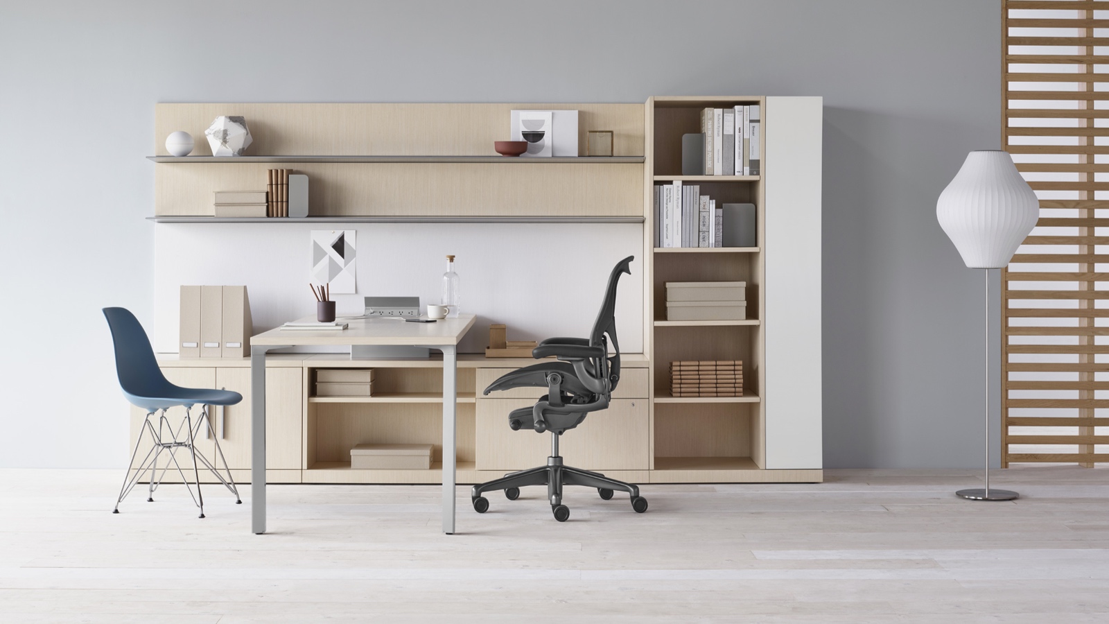 A Canvas Private Office with light wood storage, upper shelves, a black Aeron office chair, and a blue Eames Molded Plastic side chair. Select to go to the Private Workspaces page within the Canvas Lookbook.