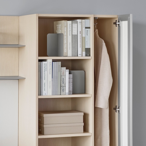 A close-up image of a light wood storage tower containing books, boxes, and a hanging coat.