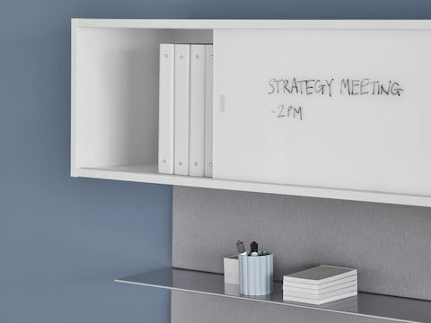 A close-up image of white, writable overhead storage with an aluminum shelf underneath.