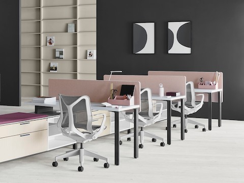 Una estación de trabajo Canvas Storage en madera clara con pantallas rosa y sillas para oficinas Cosm gris claro. Una estación de trabajo Canvas Storage en madera clara con pantallas rosa y sillas para oficinas Cosm gris claro.