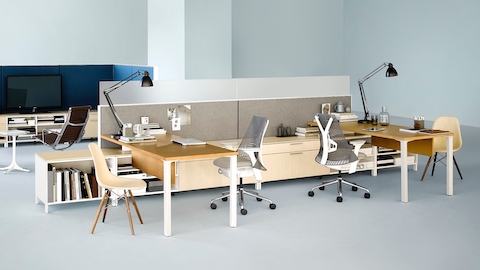 An office with a Canvas Storage workstation in light wood with grey screens and white Sayl office chairs and a lounge area nearby.