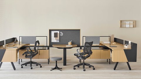 Una estación de trabajo Canvas Vista en madera clara y negro con pantalla de recato, panel de tela gris, y silla para oficinas Cosm negra.