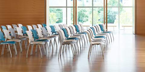 Blauwe, witte en grijze Caper stapelbare stoelen in een grote ruimte met ramen.