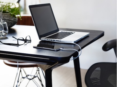 A smartphone and laptop computer charging atop a black Carafe Table.