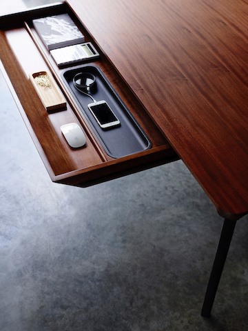 The main drawer of a medium wood Carafe Table, open to reveal a charging smartphone and other items inside.