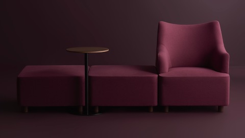 A purple Plex sectional bench with a Plex table and Plex armchair in a room with low lighting and dark purple walls and floor.