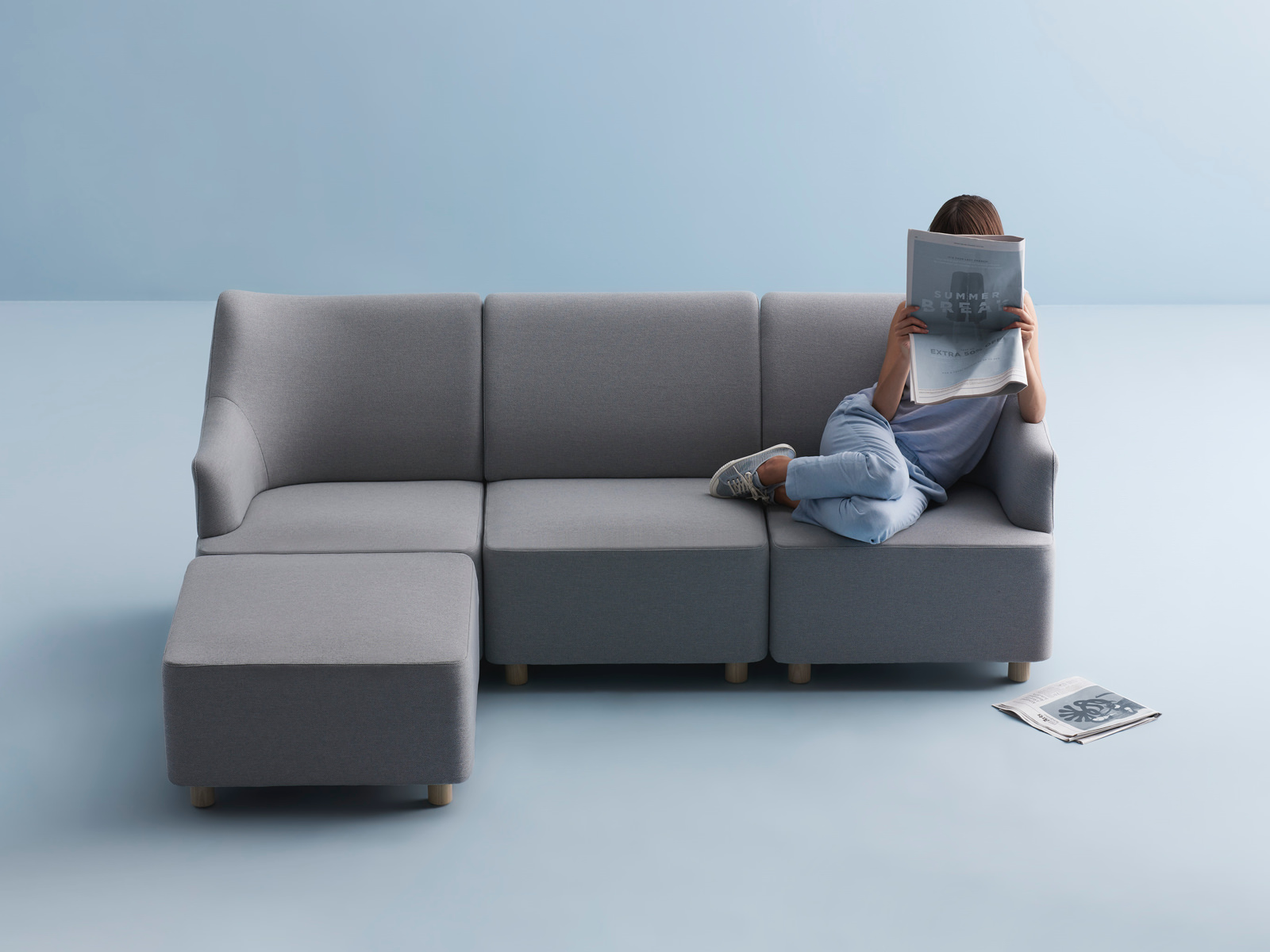 Woman reading a newspaper on gray, modular Plex Lounge Furniture.