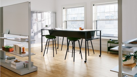 A black double sided OE1 Communal Table with castors, with OE1 Agile Walls in the foreground and OE1 Wall Rail and Board and OE1 Storage Trolley in the background.