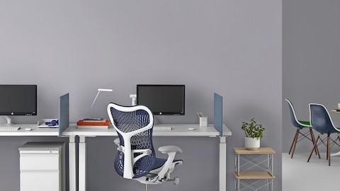 Um par de mesas brancas Renew Sit-to-Stand com telas azuis, monitores de computador e uma cadeira Mirra 2 azul.