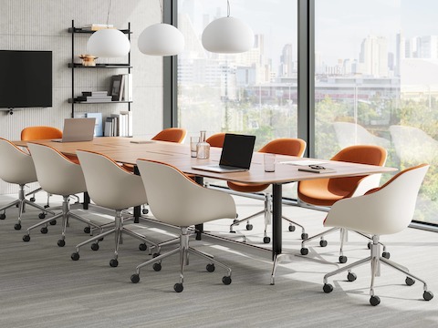 Een heldere ruimte voor videoconferenties met uitsparingen voor stroom die elke gebruiker aan de tafel gemakkelijk van stroom voorziet. De Civic-tafel wordt omgeven door tien oranje HAY AAC 252-stoelen.