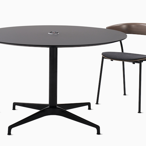 Een geheel zwarte, ronde Civic-tafel met daarnaast een notenhouten Leeway-stoel.