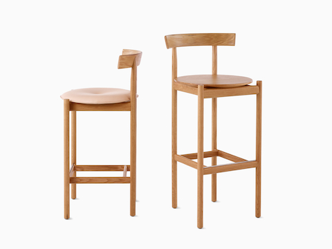 An oak counter-height Comma Stool with an upholstered seat next to an oak bar-height Comma Stool.