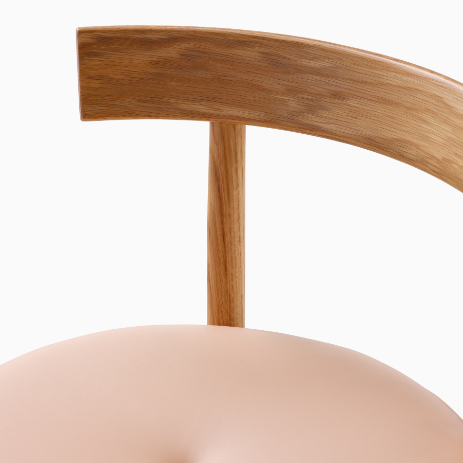 Een close-up detailopname van de beklede zitting en houten rugleuning van een Comma-kruk.