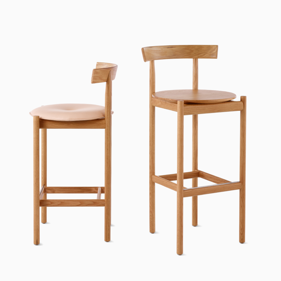 An oak counter-height Comma Stool with an upholstered seat next to an oak bar-height Comma Stool.