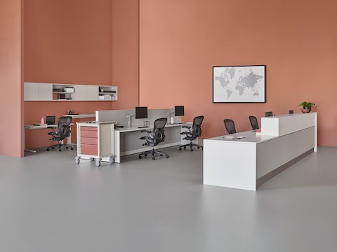 A caregiver environment setting with a white and gray prefab Commend Nurses Station, Renew Sit-to-Stand Tables, and Aeron Chairs.