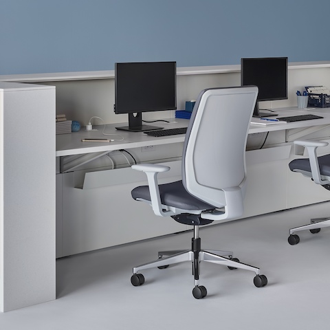 Vista interior de un mostrador de enfermería Commend prefabricado con una superficie de trabajo blanca, superficies de transacción en Corian blanco, sillas Verus y pedestales para monitor.