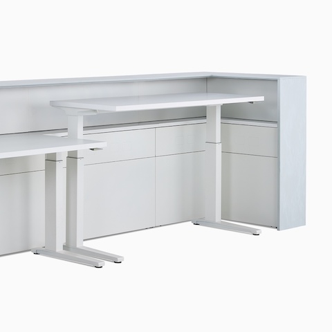 Two white Renew Sit-to-Stand Tables at differing heights tucked within the interior of a Commend Nurses Station.