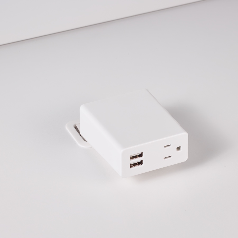 Primer plano de la abrazadera Logic Mini con dos puertos USB y un tomacorriente integrados en la tapa de una superficie de trabajo laminada de color blanco.