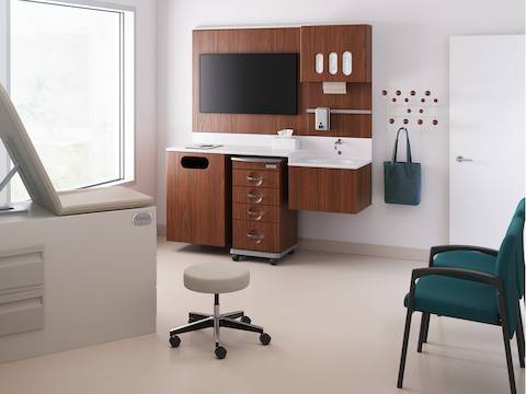 用带有中级胡桃木饰面的Compass固定工作系统布置的诊疗室，包含一辆用品车、一张检查桌、带有棕黄色椅座的内科医生凳，以及两张绿色的Valor单椅。