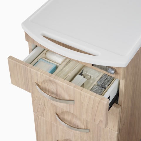 A close-up view of medical supplies in an open drawer on a Compass casework supply cart in a warm elm finish.
