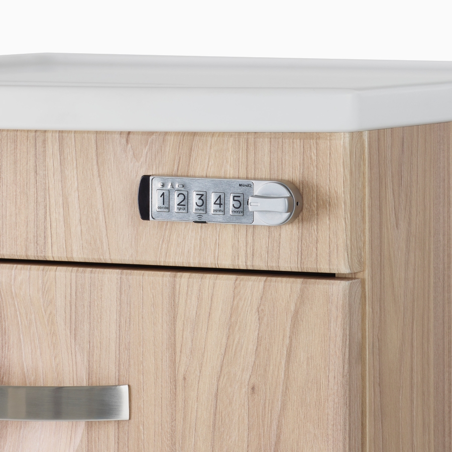A close-up view of a keyless lock on a Compass casework supply cart in a warm elm finish with a white solid surface top.