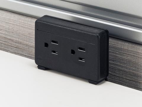 A black, two-outlet Connect Electrical Distributor attached to the back of a white work surface.