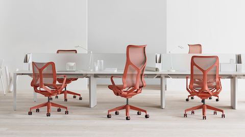 A variety of low-back, mid-back, and high-back Cosm Chairs in Canyon red at a series of bench workstations with personal lighting and privacy screens.
