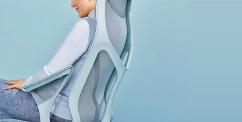 Une femme vêtue d'un pantalon en lin bleu et d'un pull bleu clair se détend dans une chaise de bureau Glacier bleu clair Cosm à dossier haut ergonomique.