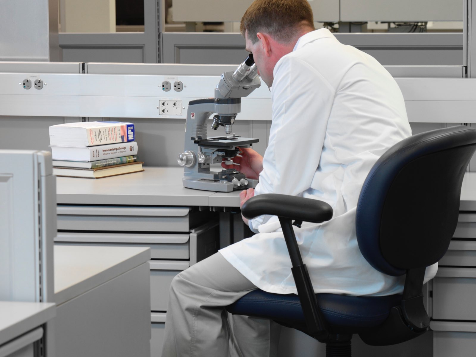 A lab technician peers through a microscope situated atop Co/Struc System modular storage drawers.