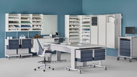 Pharmacy with white Co/Struc System of dispensing shelves, lockers, process tables, L Carts with blue drawers, a technology cart with blue drawers and a Sayl Stool.