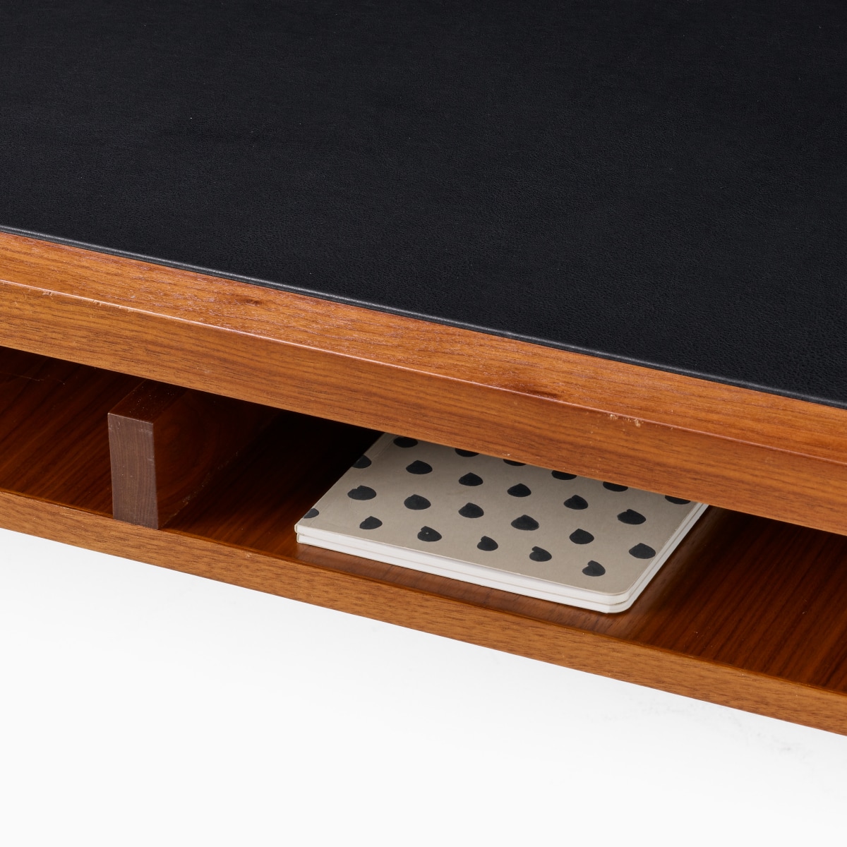 Detail of the secondary storage shelf of the Eames 2500 Series Executive Desk in walnut, and a white journal.