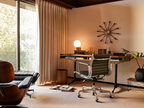 An Eames 2500 Series Executive Desk in walnut and black leather inlay and Eames Aluminium Group Chair, Tip of the Tongue Lamp, Eames Lounge and Ottoman and Nelson Spindle Clock, Risom Wastebasket, and Eames Wire Base Low Table