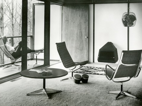 Black Eames Aluminum Group lounge chairs and a round Eames occasional table in a residential setting.