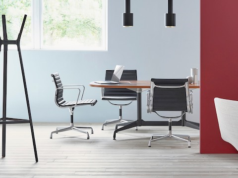 Eamesテーブルの周りに黒のEames Aluminum Groupのミッドバックチェアがある会議室。