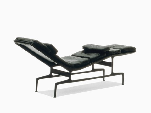 Three-quarter rear view of a black leather Eames Chaise, emphasizing the die-cast aluminum frame.