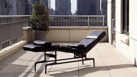 Um couro preto Eames Chaise situado em uma varanda com vista para um horizonte urbano.