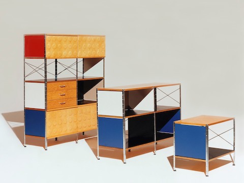 Tres unidades de almacenamiento Eames de varios tamaños, todas en esquemas de colores brillantes con acentos de abedul, azul, rojo, negro y blanco.