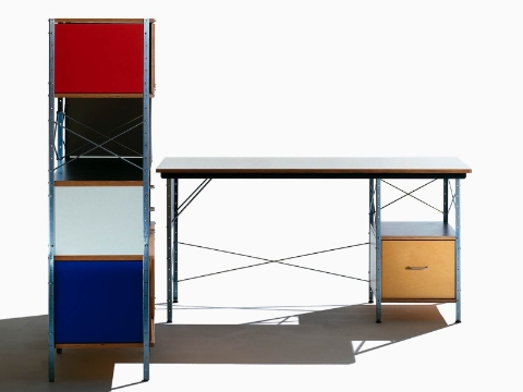 Uma vista frontal de uma mesa Eames em cores neutras ao lado de uma unidade de armazenamento Eames com detalhes brilhantes, mostrada de lado.