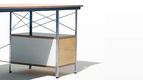 Uma vista em ângulo de um Eames Desk com detalhes de bétula, branco e azul, enfatizando os suportes cruzados de aço.