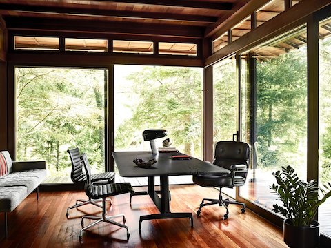 Oficina privada equipada con una silla ejecutiva Eames negra, una mesa AGL negra y dos sillas negras Eames Aluminum Group.