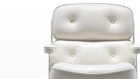 Primer plano del detalle del botón en el cojín trasero de felpa de una silla ejecutiva Eames de cuero blanco.