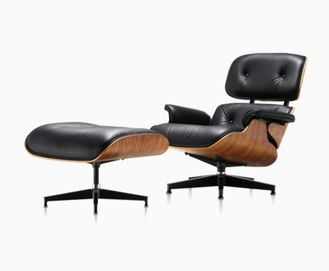 Sillón de cuero y otomana Eames de cuero negro con una carcasa de chapa de madera, vista desde un ángulo de 45 grados.