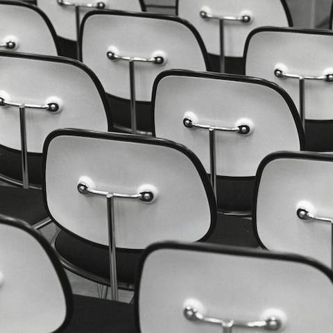 Mass of Eames Molded Plastic Dining Chairs facing away with white backs and a metal frame.