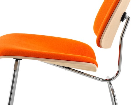 Close profile view of an Eames Molded Plywood Chair with orange upholstery and chrome-plated legs. Close profile view of an Eames Molded Plywood Chair with orange upholstery and chrome-plated legs.